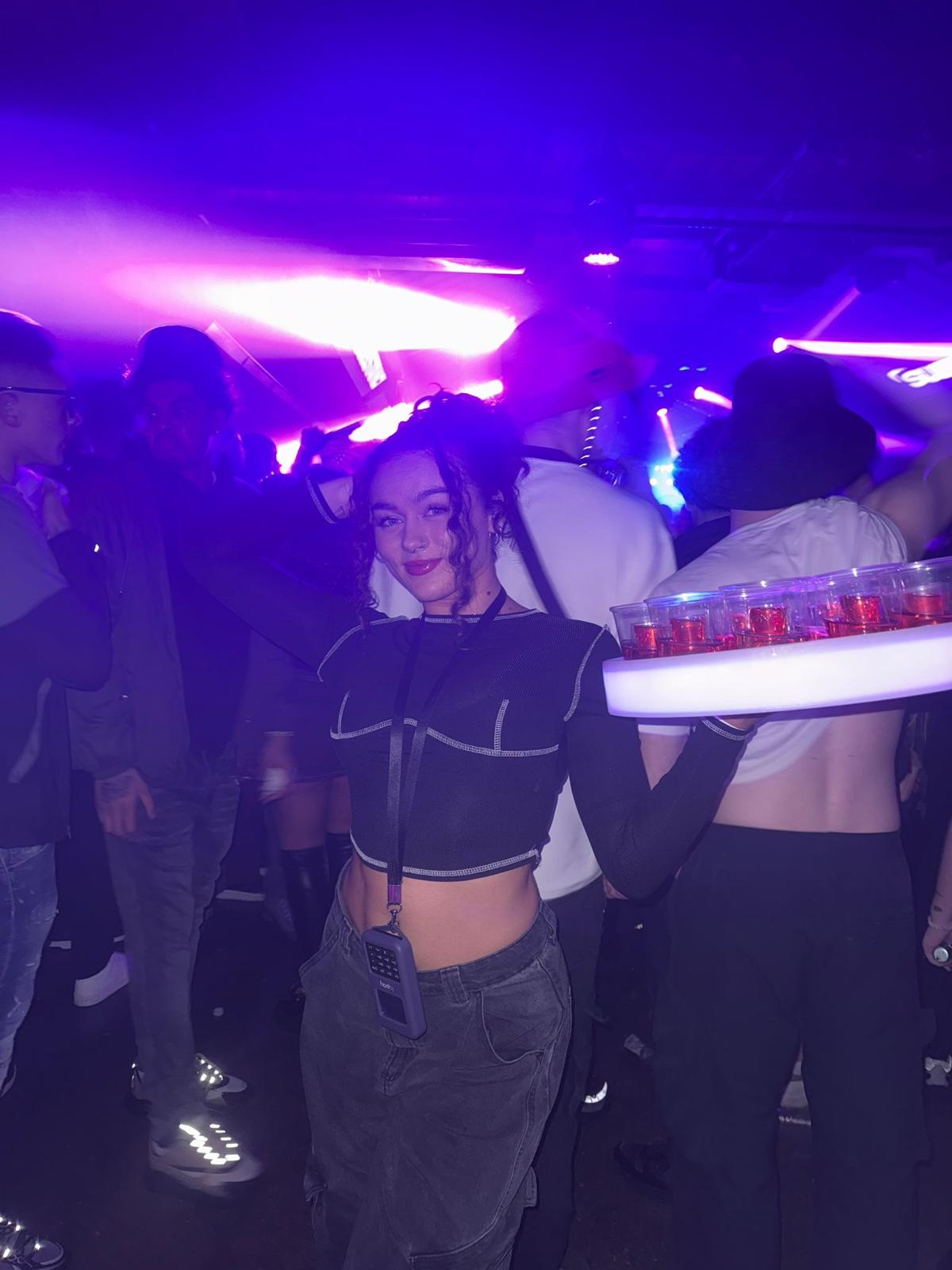 Reign shot seller with LED tray on a neon-lit dancefloor