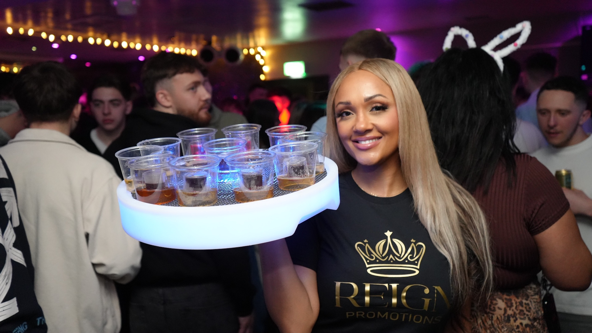 Reign shot seller with an illuminated tray in a packed venue
