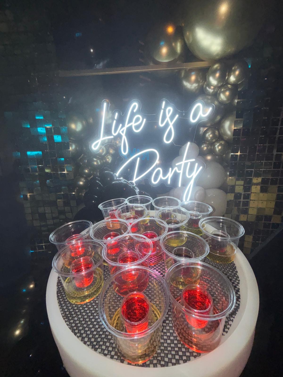 Reign shot tray under a Life Is A Party neon sign